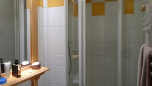 Un baño con cabina de ducha de vidrio, un estante de madera con artículos de aseo y una toalla colgada en la pared.