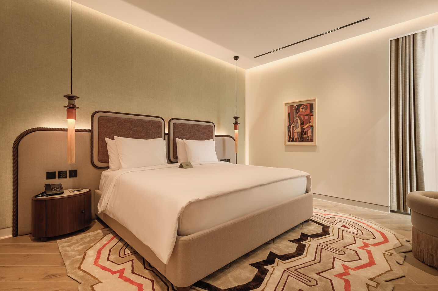 Una habitación de hotel moderna con una cama grande, mesitas de noche, un escritorio y un cuadro en la pared.