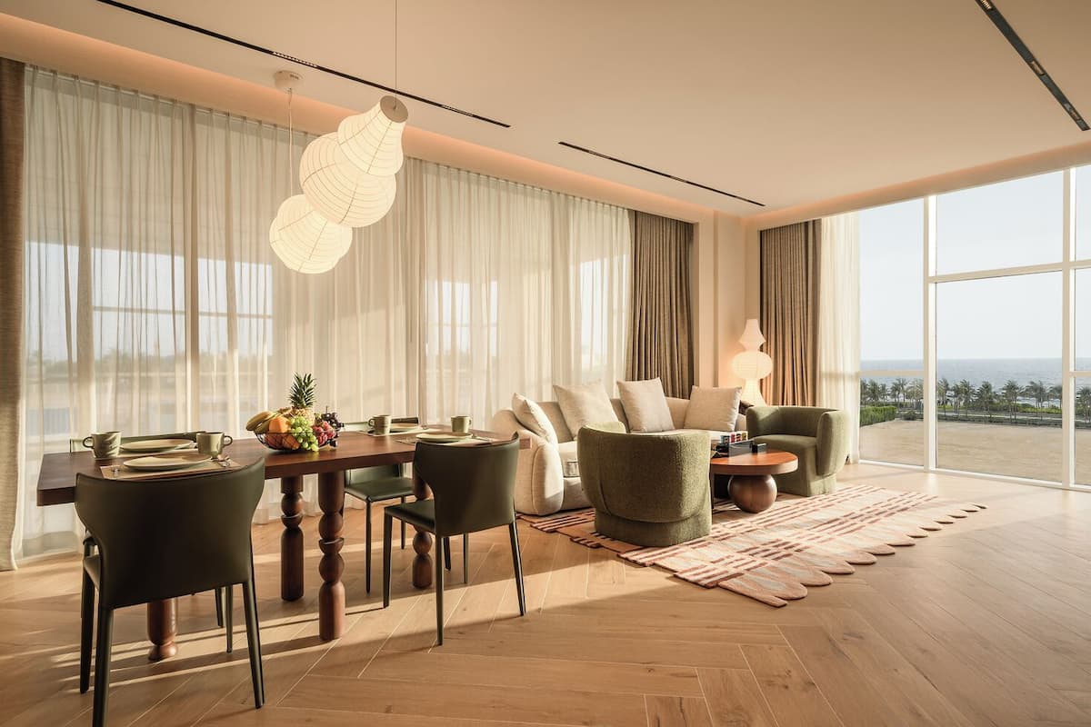 Una sala de estar moderna con comedor, ventanas amplias con cortinas y vista a la playa.
