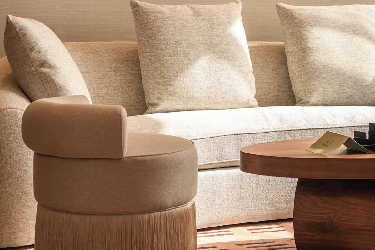 Una sala de estar moderna con un sofá color beige, un reposapiés a juego y una mesa de centro de madera. Hay cuadros abstractos en la pared.