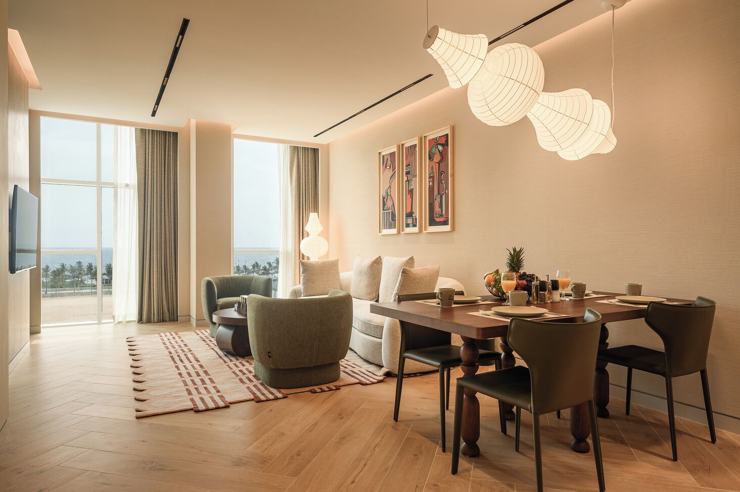 Habitación de hotel moderna con zona de comedor, sofá, televisión y un amplio ventanal con vistas.