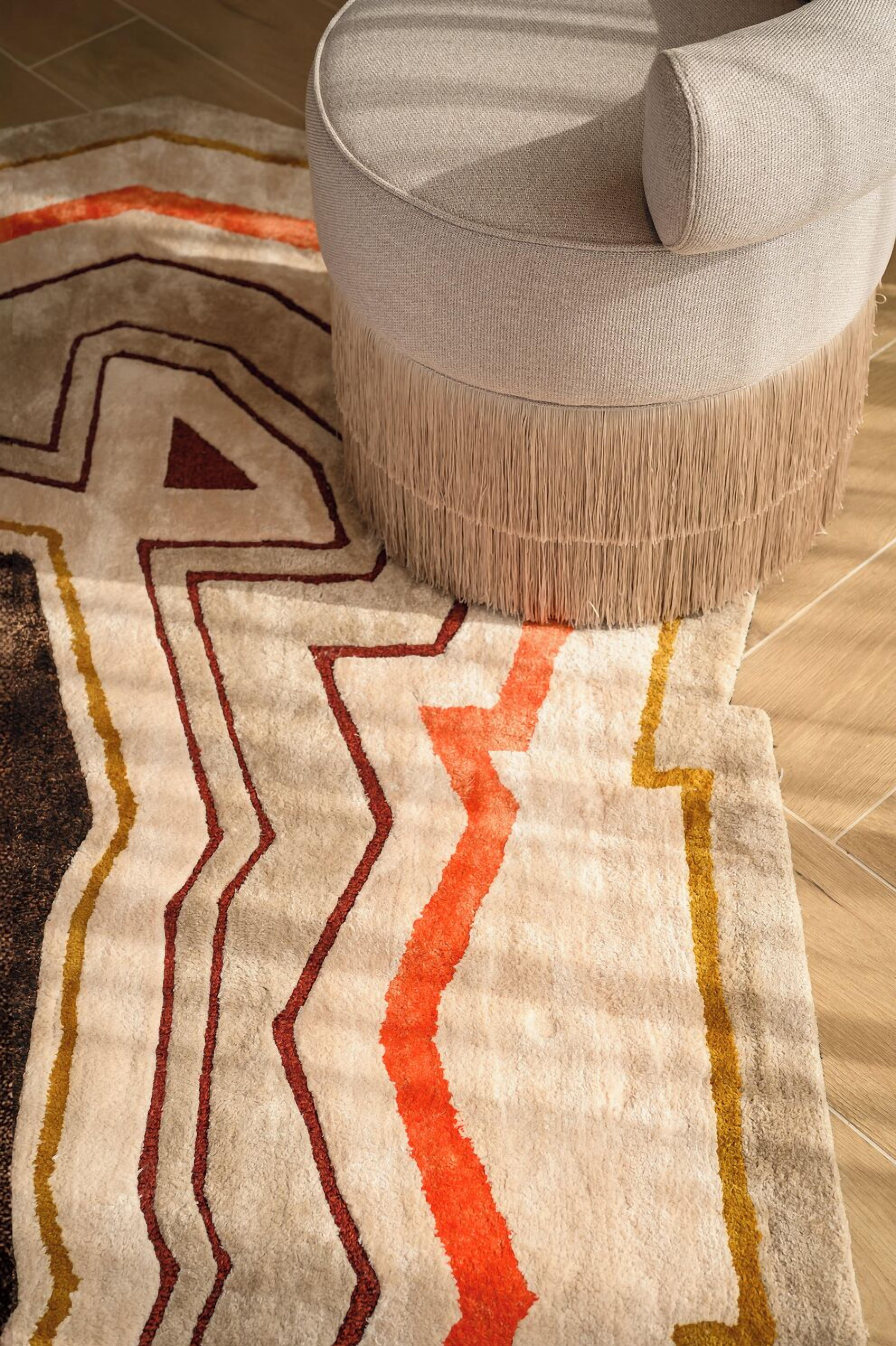 Ein runder, strukturierter Ottomanen mit Kissen darauf, platziert auf einem Teppich mit Zickzack- und Chevron-Mustern.