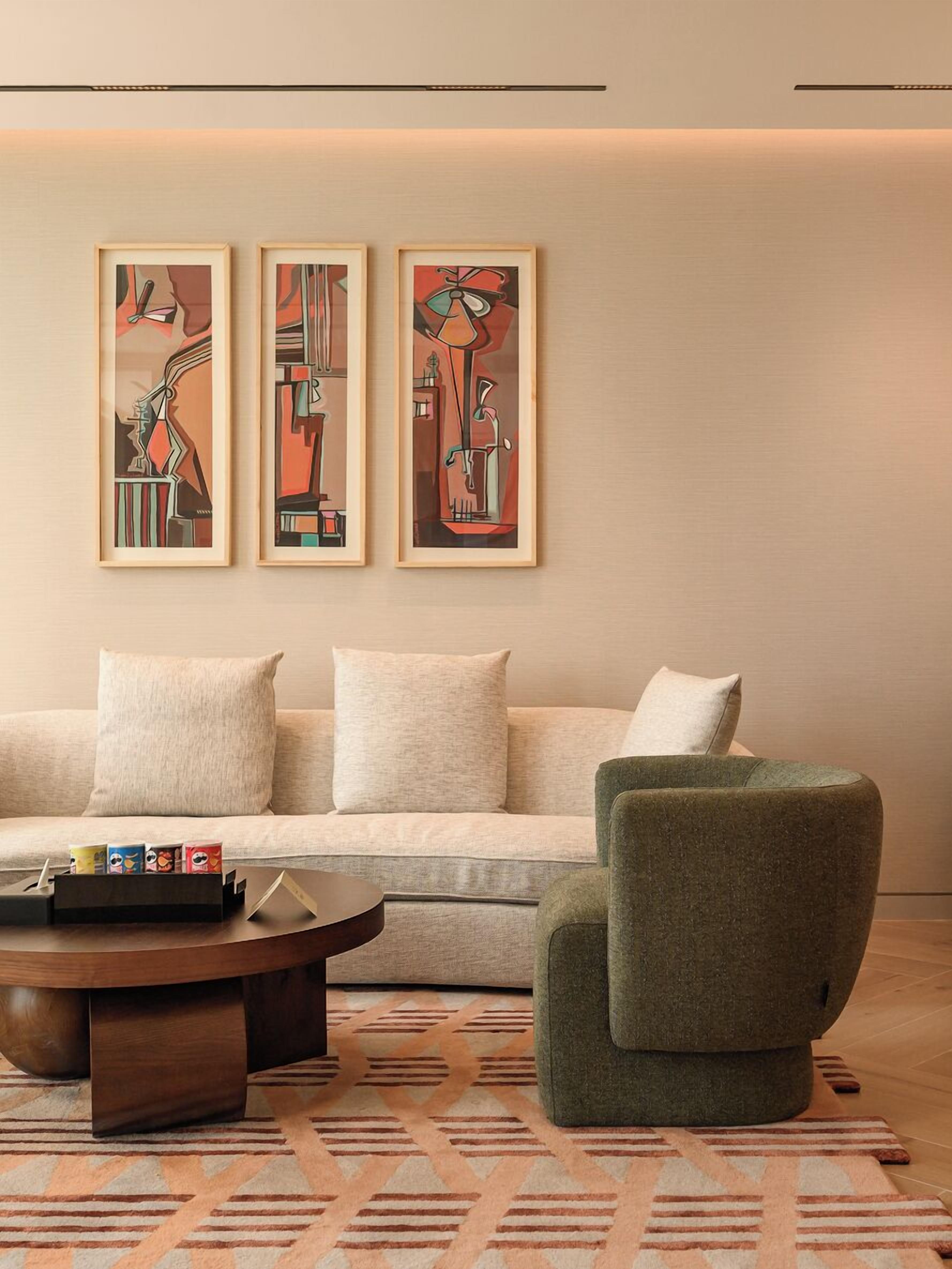 A modern living room with a sofa, a green armchair, and a coffee table. There are three abstract paintings on the wall.