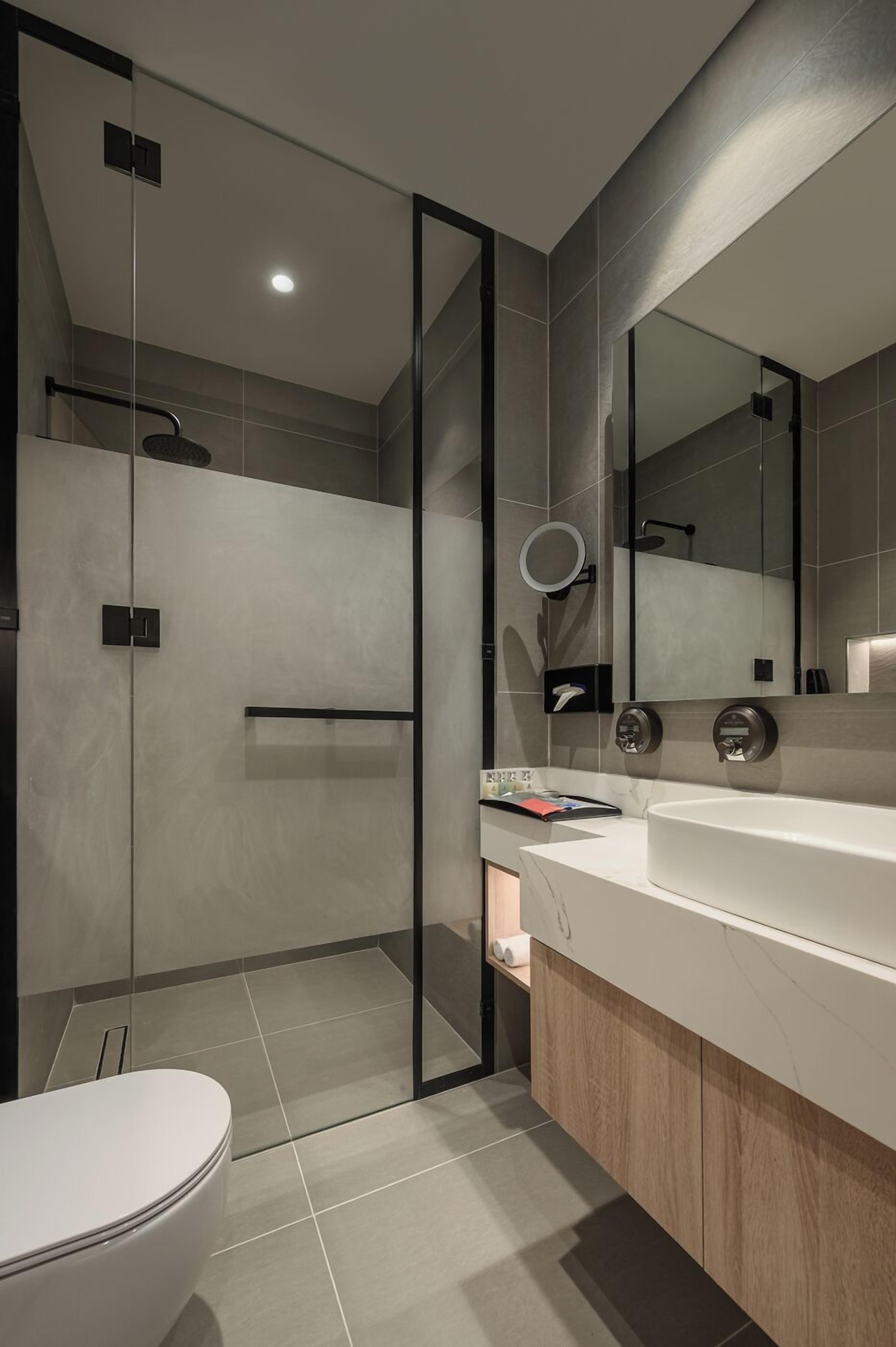 Un baño moderno con cabina de ducha de vidrio, un espejo grande y un lavamanos blanco.