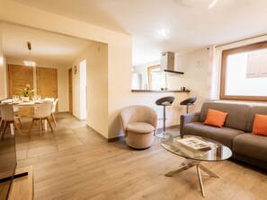 Ein modernes Wohnzimmer mit einem Glastisch, einer Couch mit orangefarbenen Kissen und einem Essbereich mit Holztisch und Stühlen.