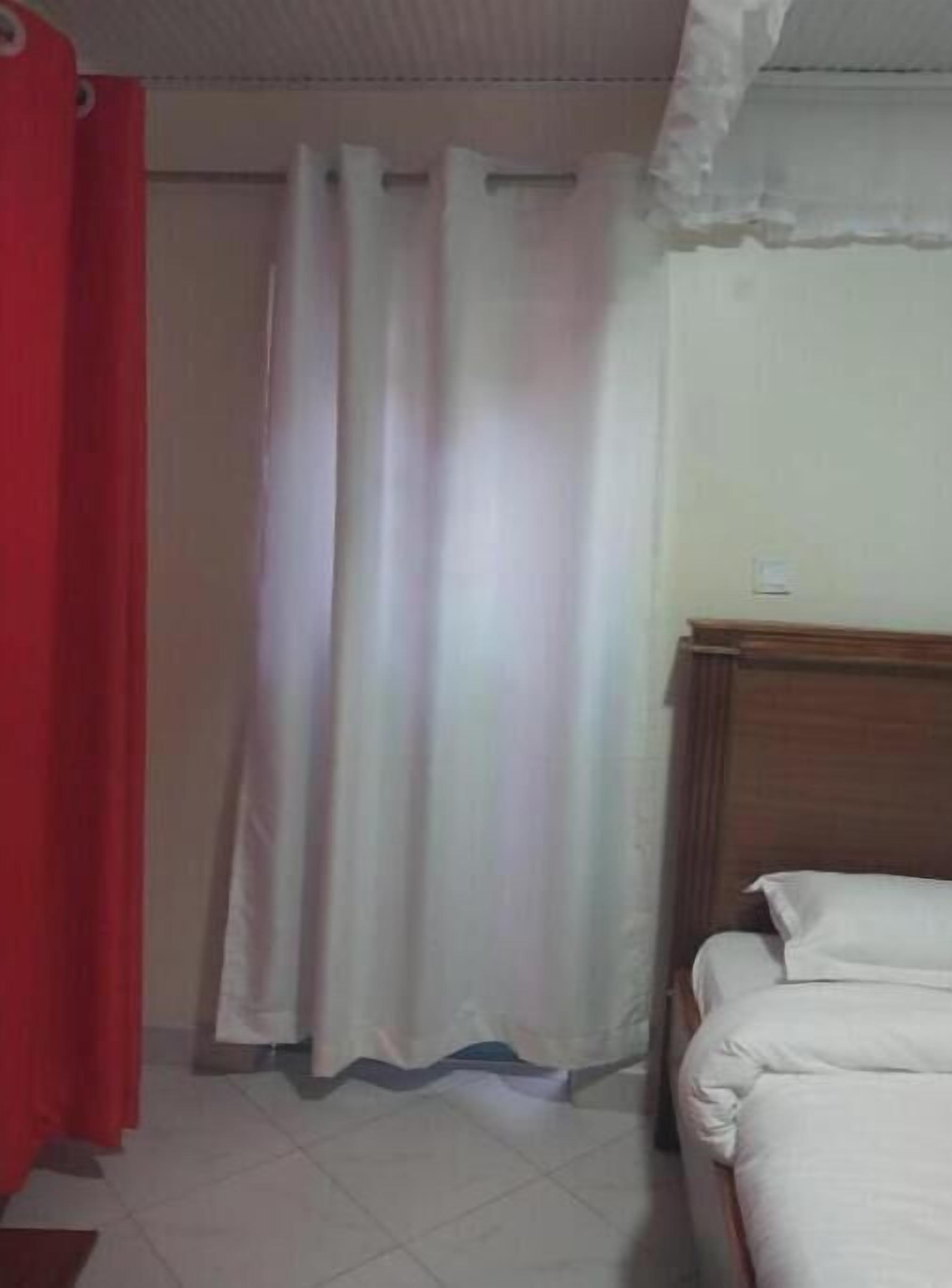 Une chambre avec un lit, une tête de lit en bois, un rideau rouge et un rideau blanc.