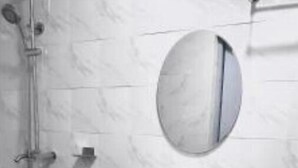 Une salle de bain avec un lavabo sur colonne blanc, un miroir rond et une douche équipée d’un pommeau de douche à main.