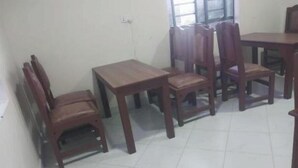 Un espace repas avec des tables et des chaises en bois, une fenêtre avec des stores et un sol carrelé.