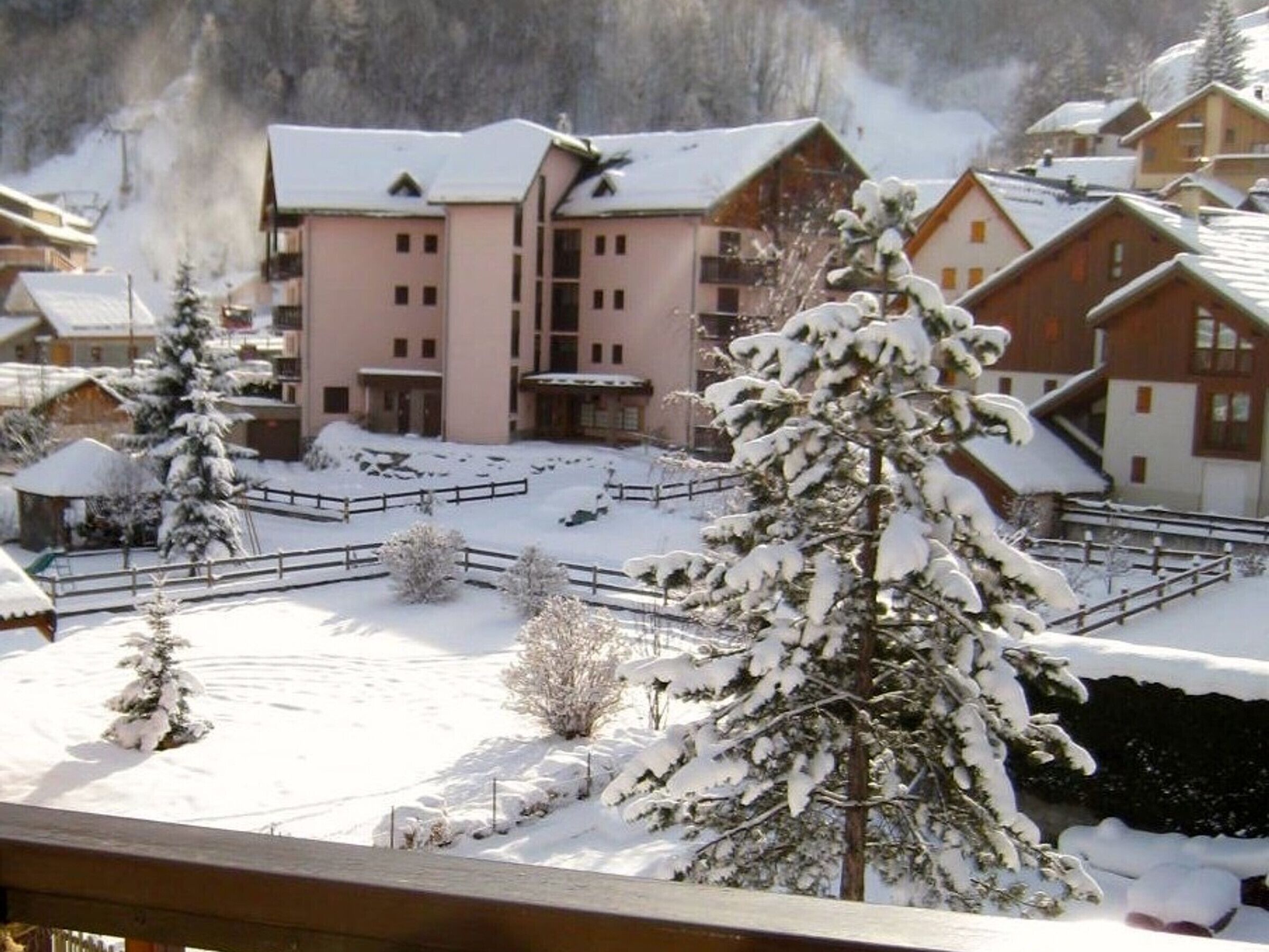 A snow-covered village with wooden buildings and a large pink hotel in the background.