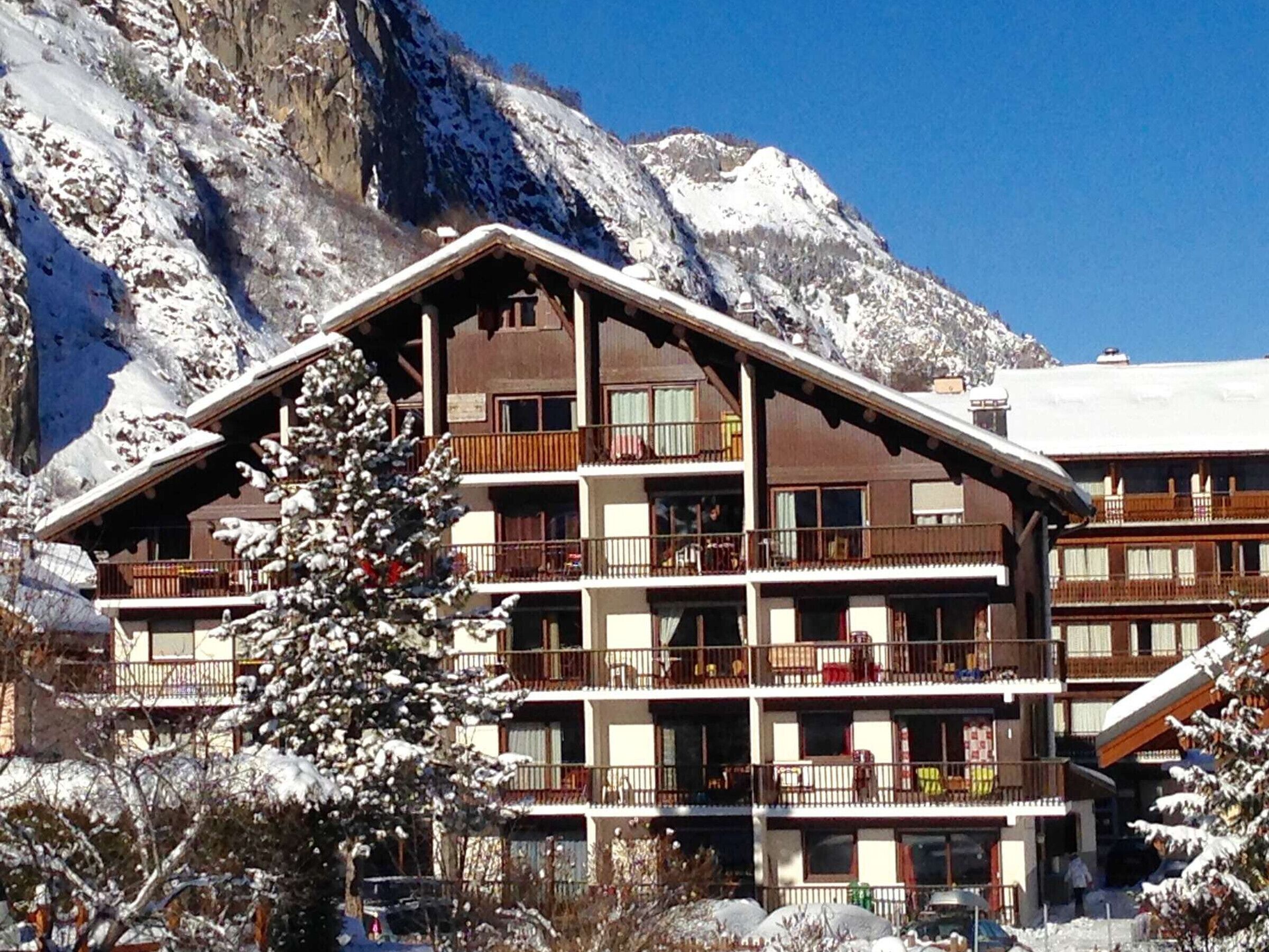 Un hôtel à plusieurs étages, doté de balcons, qui se dresse sur fond de montagnes enneigées.