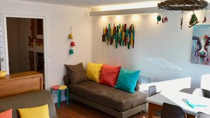 Ein modernes Wohnzimmer mit einer Couch, einem Esstisch und Stühlen. Außerdem steht ein kleiner Hocker und ein Holzschrank da.