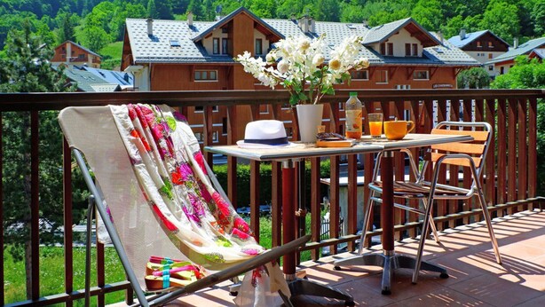 Ein Balkon mit einem Stuhl, Tisch und Blumentöpfen.