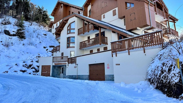 Ein mehrstöckiges Hotel mit hölzernen Balkonen und einer Skipiste im Hintergrund.