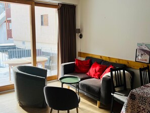 Ein gemütliches Zimmer mit einer Couch, zwei Sesseln, einem kleinen Tisch und Blick auf einen Balkon.