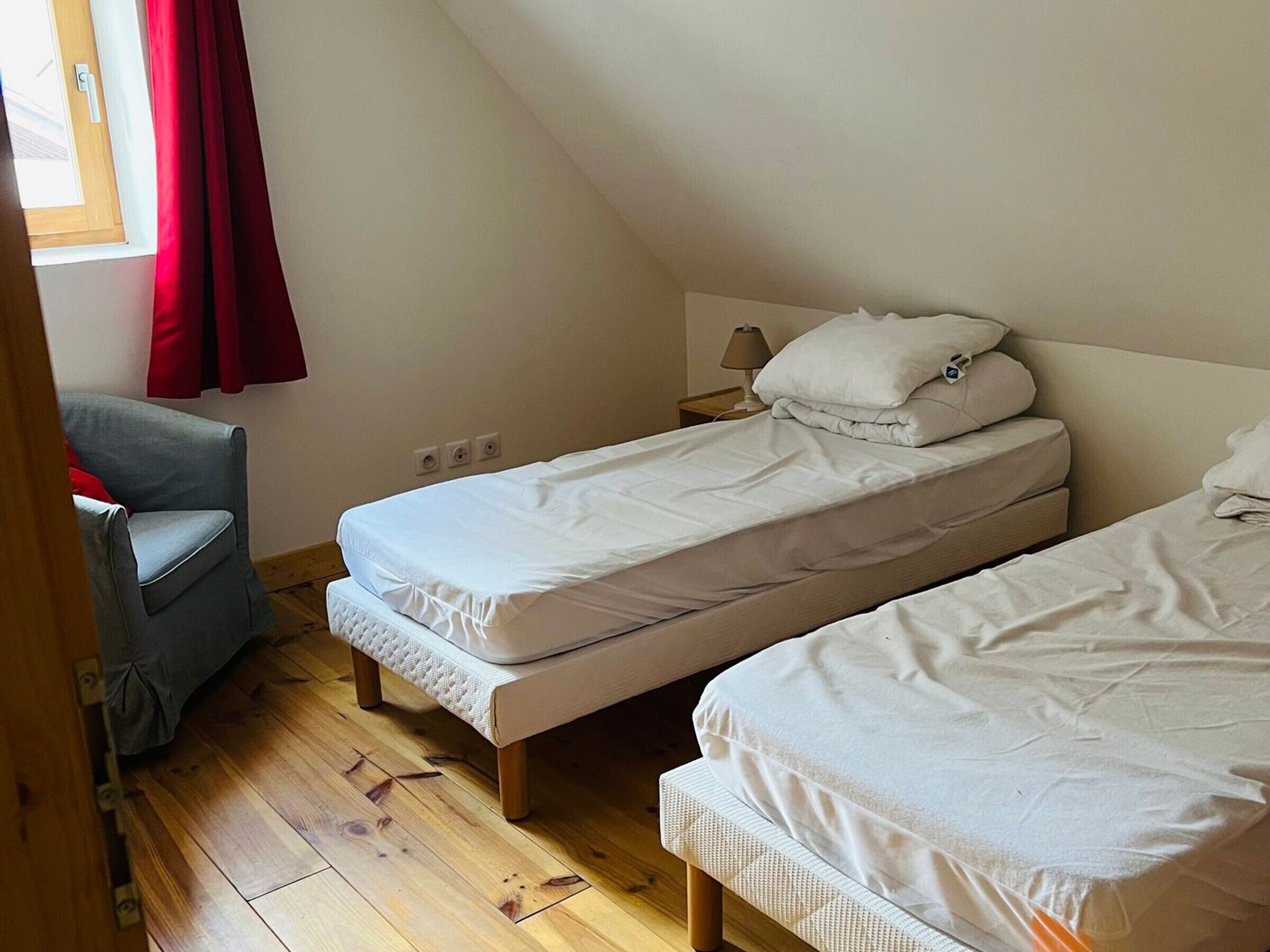 Une chambre avec deux lits simples, une chaise et une fenêtre avec des rideaux rouges.