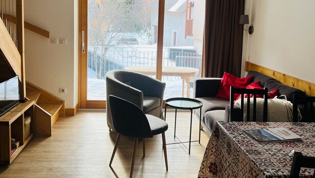 A modern living room with a sofa, two armchairs, a small table, and a TV. There is a sliding glass door leading to a balcony with a view of the outside. - Triplex 3 rooms with loft, 6 people, terrace, private parking (Valloire)
