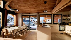 A modern kitchen with a central island, wooden beams on the ceiling, and large windows offering a view of the outside. - Spacious chalet for 11, 4 rooms, parking, sunny terrace (Valloire)