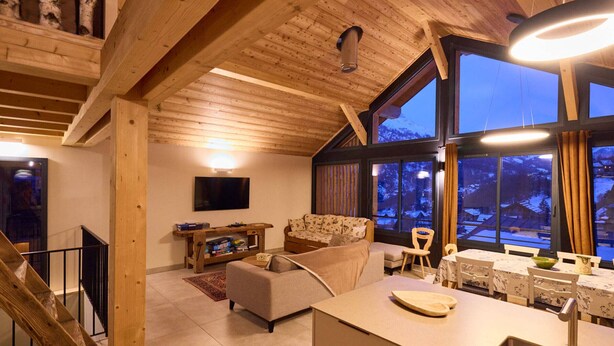 A cozy cabin interior with a wooden ceiling, a sofa, a dining table, and a kitchen area. - Spacious chalet for 11, 4 rooms, parking, sunny terrace (Valloire)