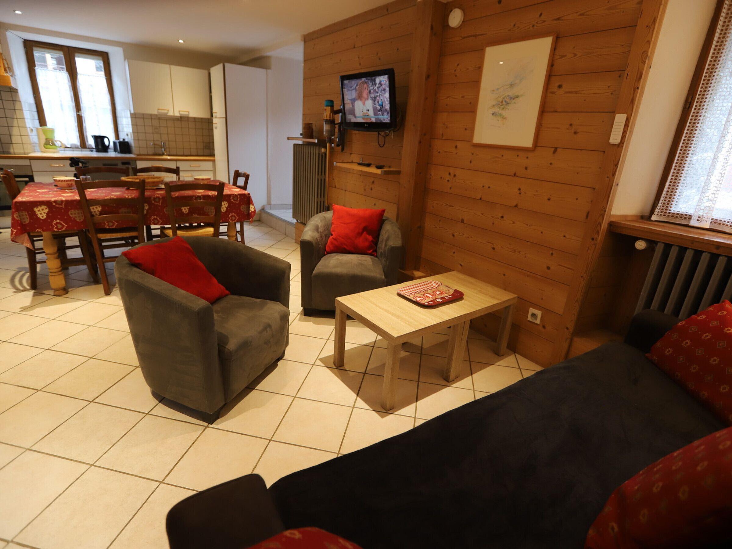 A cozy living room with a sofa, two armchairs, a coffee table, and a television mounted on a wooden wall.