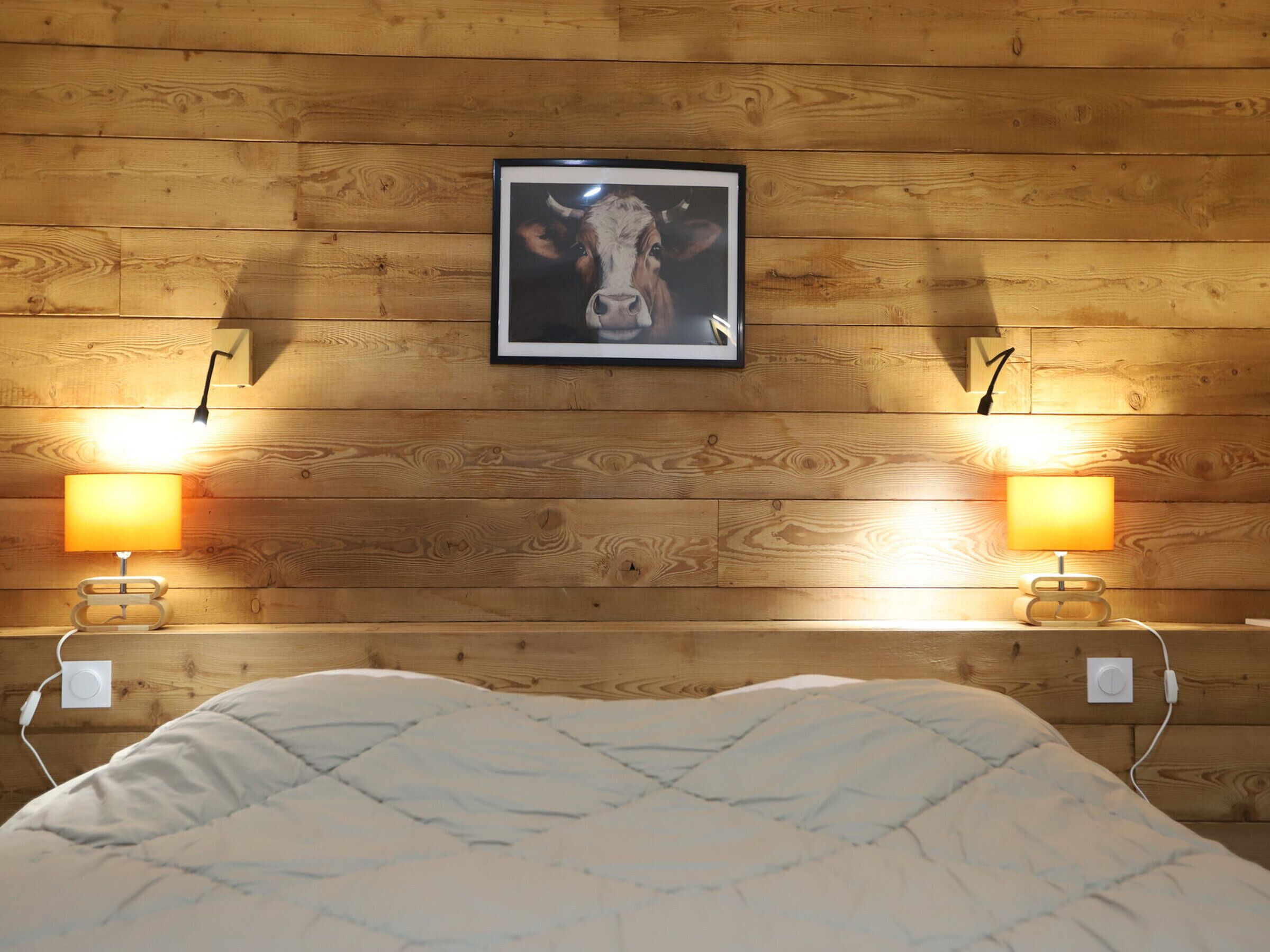 A wooden-paneled room with a bed, two bedside lamps, and a framed picture on the wall.