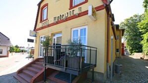 Un bâtiment jaune avec un toit rouge, un balcon doté d’une rambarde en métal et un escalier menant à l’entrée.