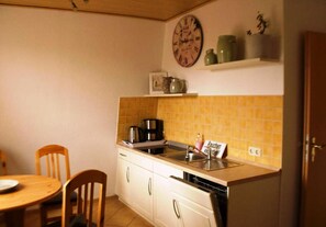 A small kitchen with a sink, stove, and a clock on the wall. There is a chair and a table with a plate on it. - Einladende Ferienwohnung in Wiek mit Garten (Wiek)
