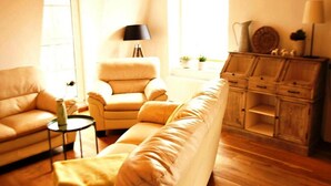 Un salon avec un canapé beige, un fauteuil assorti, une petite table d’appoint et un meuble en bois doté de tiroirs.
