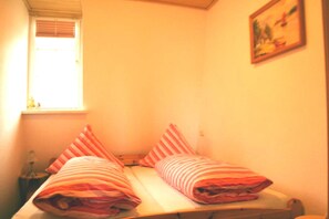 A small room with two beds, a window, and a painting on the wall. - Einladende Ferienwohnung in Wiek mit Garten (Wiek)