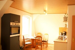 A compact kitchen with a dining table, chairs, and a built-in oven. - Einladende Ferienwohnung in Wiek mit Garten (Wiek)