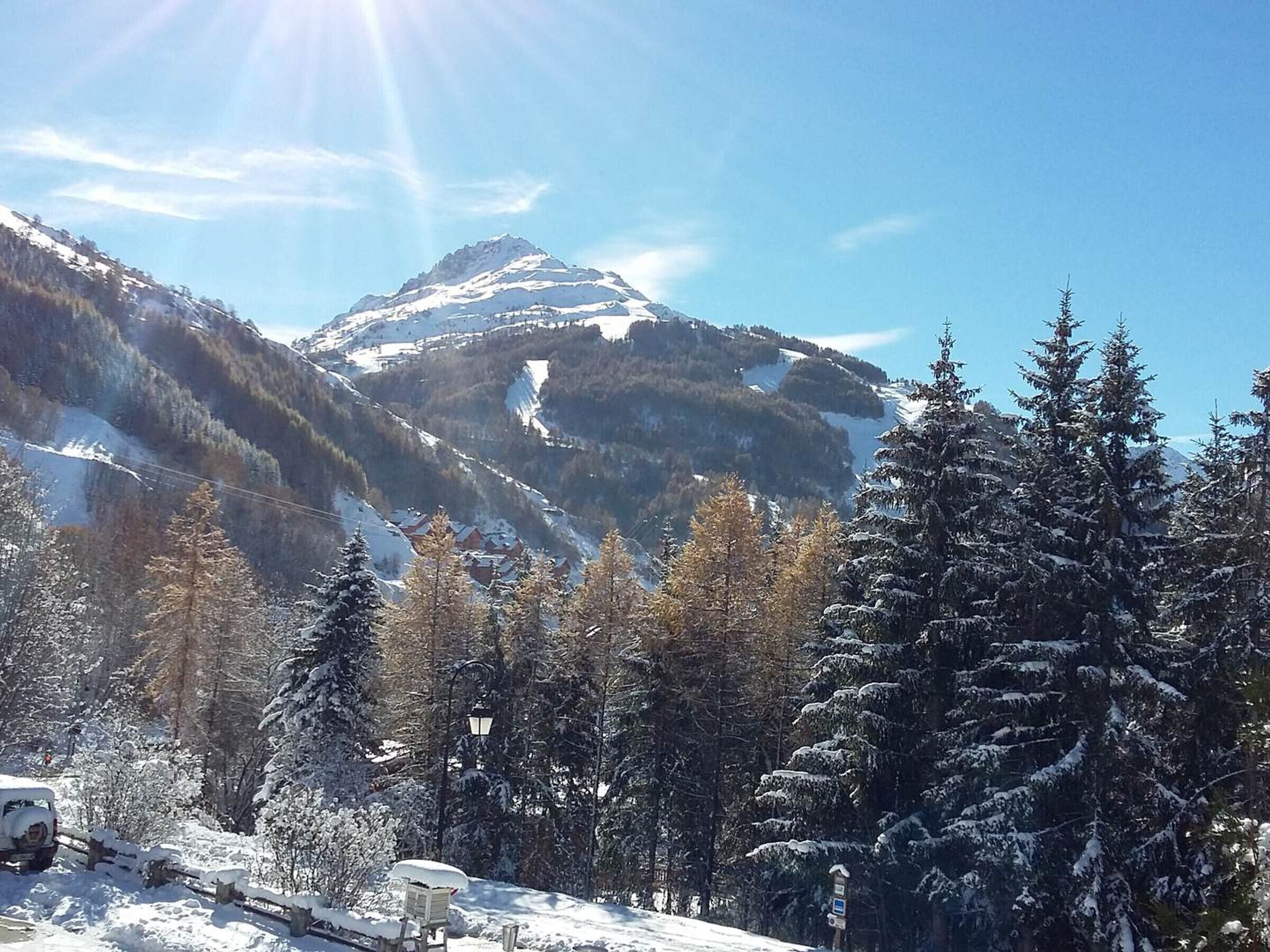 Un paysage de montagne enneigé, avec un ciel dégagé, des arbres et un véhicule.