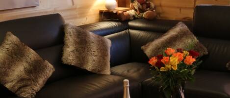 Una sala de estar acogedora con un sofá de cuero, almohadones de piel, una mesita con una botella de champán, copas y un florero.