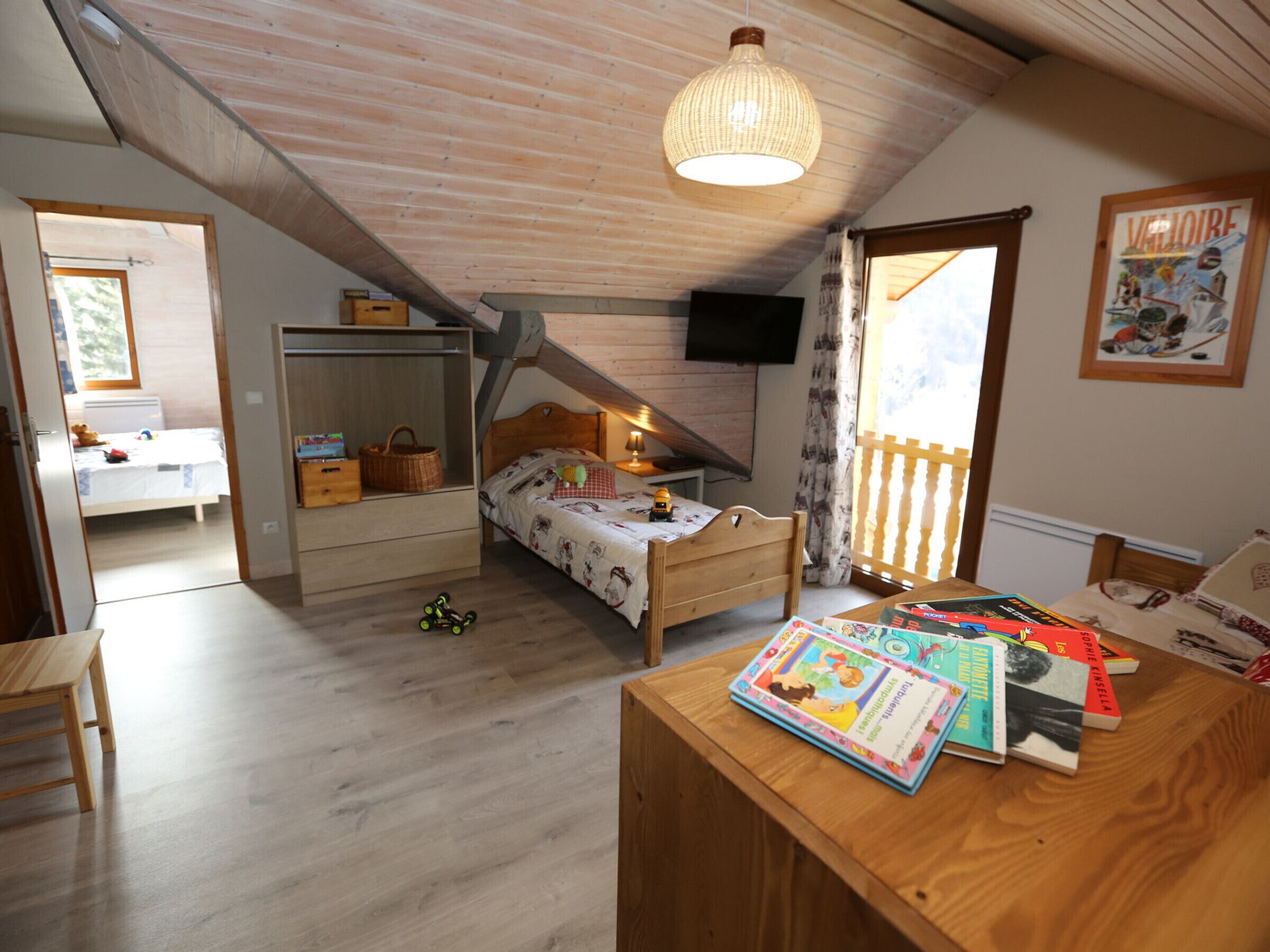 Une chambre confortable avec un plafond en pente, un lit en bois, un bureau avec des livres pour enfants et une fenêtre donnant sur un beau paysage.