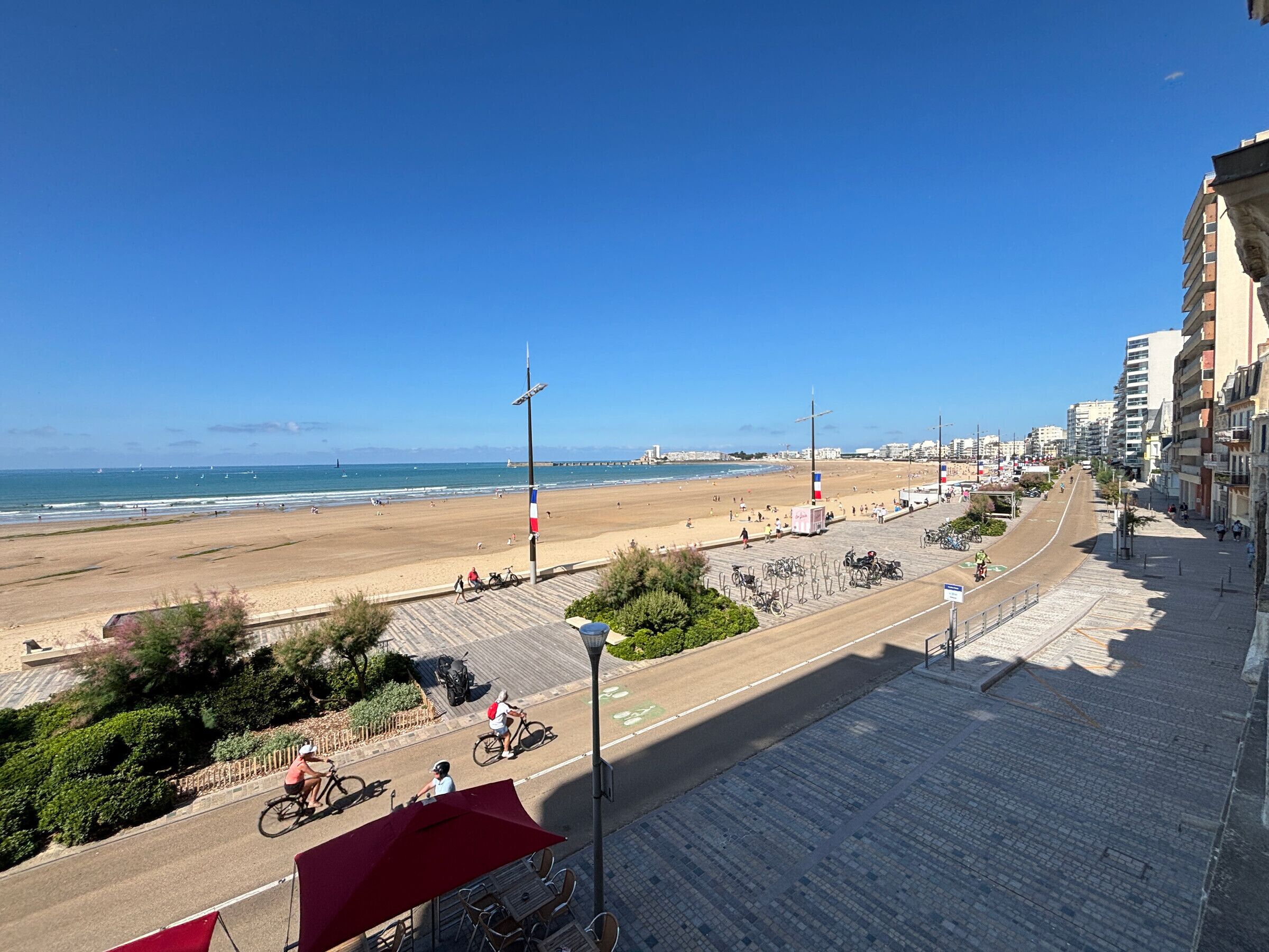 Un paisaje urbano costero con una playa, un paseo marítimo pavimentado y edificios.