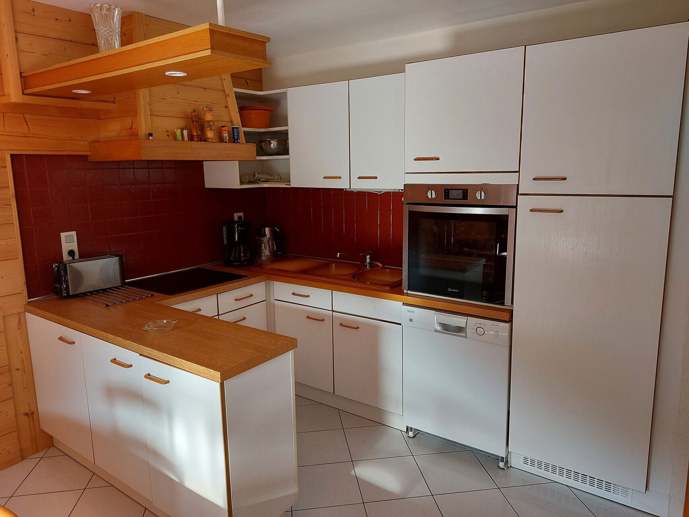 Cozinha compacta com armários brancos, bancada de madeira, forno embutido e lava-louças.