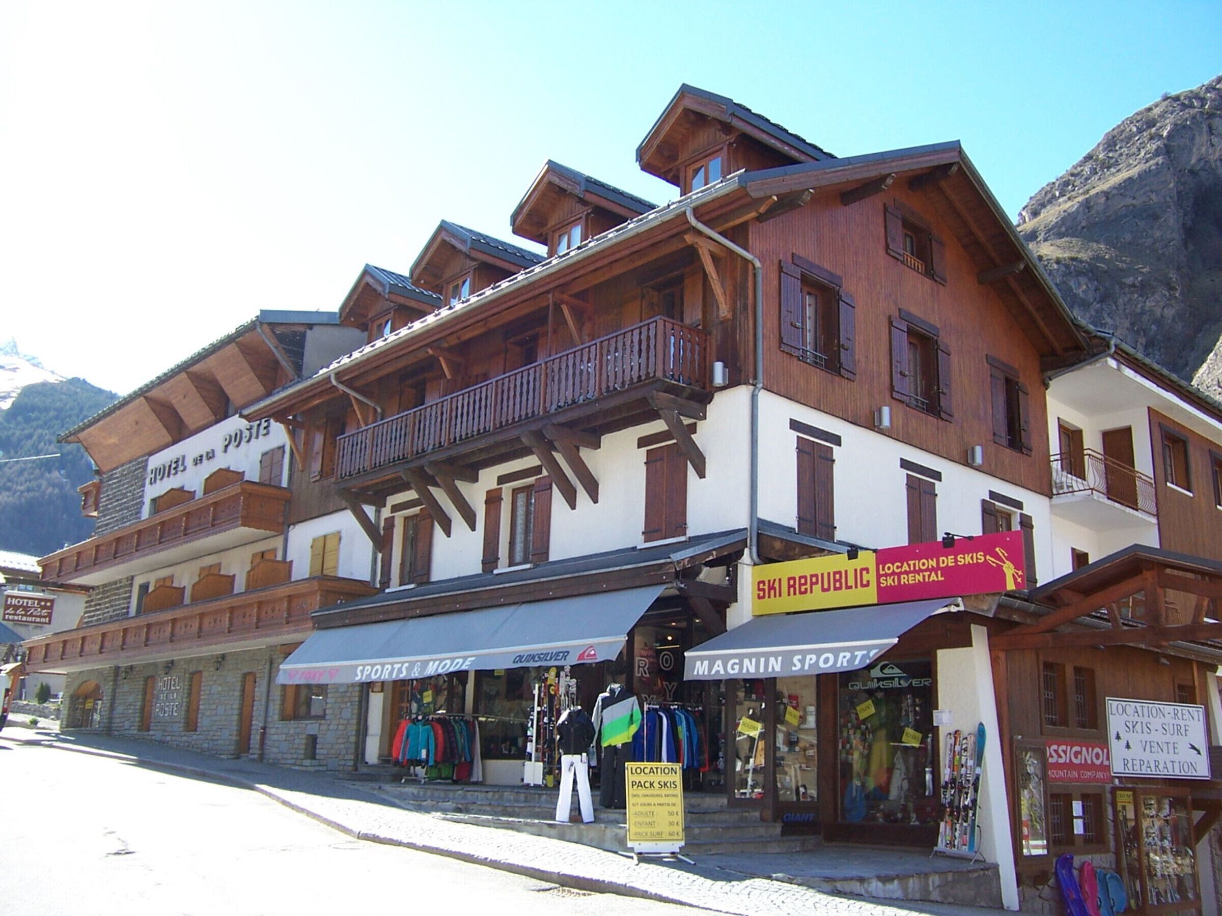 A hotel with multiple floors, wooden balconies, and a storefront with ski-related shops.