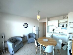 A compact living space with a kitchenette, a dining area with a wooden table and chairs, a gray sofa, and a floor lamp.