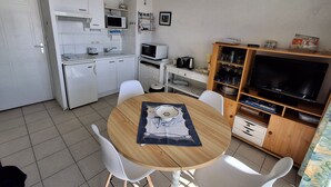 Une cuisine compacte équipée d’un four à micro-ondes, d’un grille-pain et d’un évier. On y trouve une table à manger avec des chaises, ainsi qu’un téléviseur posé sur un meuble en bois.