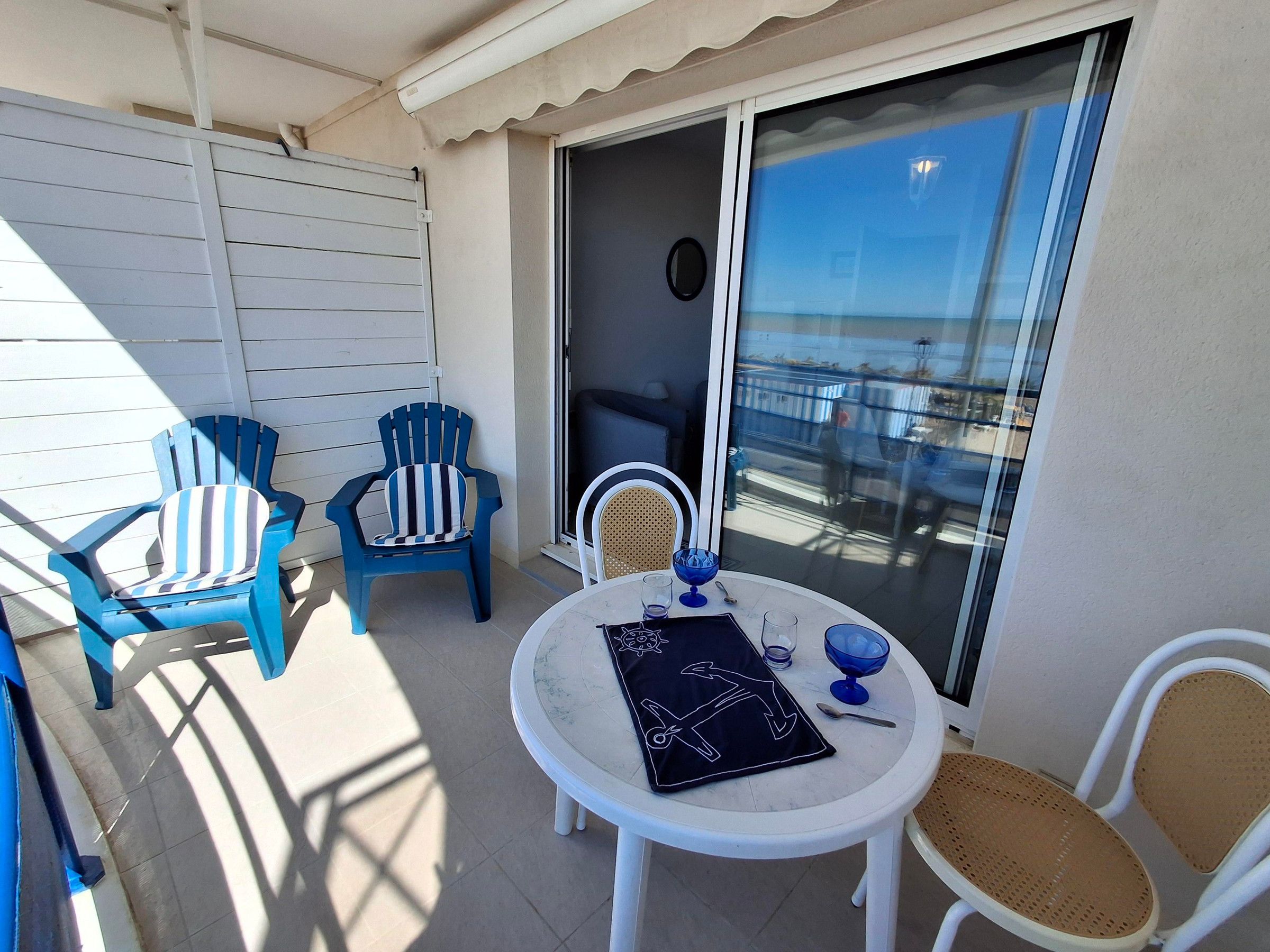 Un balcon avec deux chaises, une table et une porte vitrée donnant sur un espace intérieur.