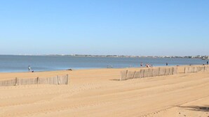 Une vaste plage de sable, avec une clôture en bois au premier plan et un ciel bleu dégagé.