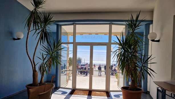L’entrée d’un hôtel, avec un sol carrelé, des plantes en pot et une porte vitrée donnant sur l’extérieur.