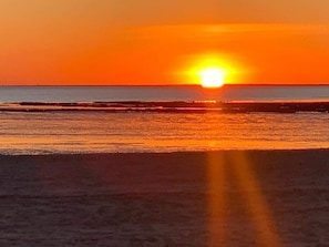Un atardecer sobre una playa con aguas tranquilas que reflejan el cielo naranja.