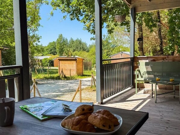 Una terraza de madera con una mesa, un plato de cruasanes y un vaso de zumo de naranja.