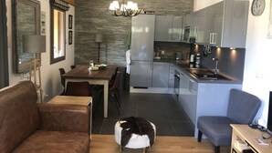 Une cuisine moderne avec des meubles gris, un coin repas avec une table et des chaises en bois, un canapé en cuir marron, un fauteuil gris et un pouf décoratif en forme d’animal.
