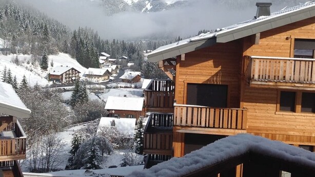 Un chalet en bois doté de balcons donnant sur un village de montagne enneigé.