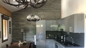 Une cuisine moderne avec un revêtement mural en pierre, des appareils en acier inoxydable et un coin repas comprenant une table et des chaises en bois.