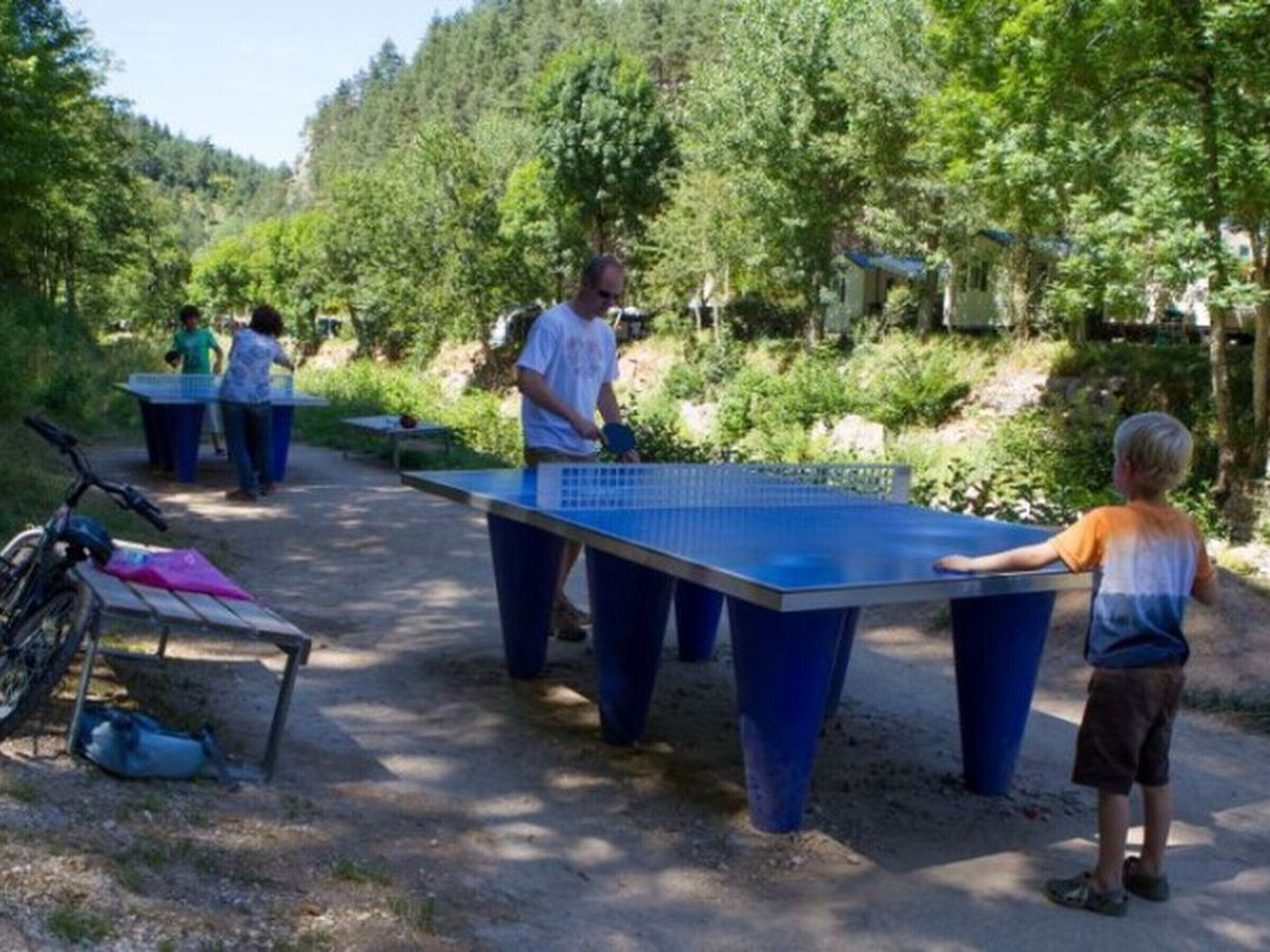 Un espace de jeu de tennis de table en plein air, avec des tables et des joueurs.