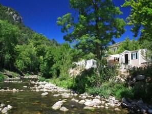 A river with rocks, a tree, and a small cabin by the water.