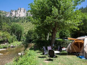 A camping site with a tent, chairs, and a river.