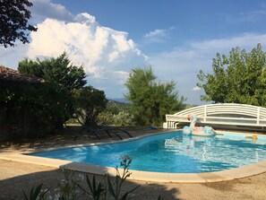 Una piscina con un puente blanco, rodeada de vegetación y árboles.
