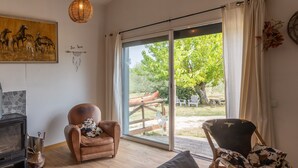 Een kamer met een open haard, een grote schuifdeur naar een buitenruimte, een schommelstoel en een wandlamp.